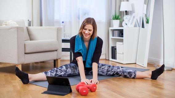 A young woman is doing sports exercises on a mat in the living room in front of a tablet.  © picture alliance / dpa Themendienst Photo: Christin Klose