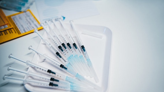 Mehrere Spritzen liegen auf einem weißen Tablett, im Hintergrund sind Papiere und ein Impfbuch zu erkennen. © Photocase Foto: David W.