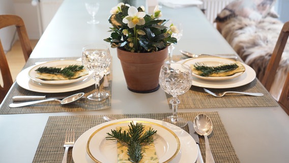 Auf weißen Tellern mit Goldrand liegen grün-goldene Papierservietten und etwas Tannengrün. © NDR Foto: Anja Deuble