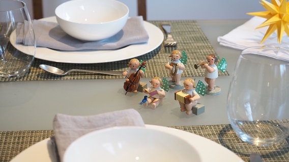 Kleine Engelsfiguren schmücken einen schlicht gedeckten Tisch mit weißem Geschirr und hellgrauen Stoffservietten. © NDR Foto: Anja Deuble