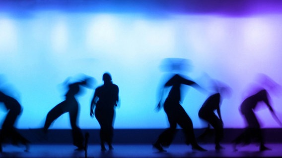 Tanzende Figuren vor blau-lila beleuchtetem Hintergrund. © iStock Foto: Dirk Freder