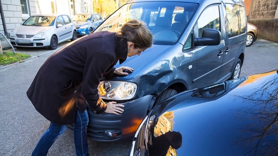Frau schaut sich verbeultes Auto an © imago 