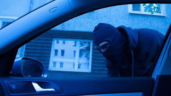 Ein maskierter Mann ist durch ein Seitenfenster an einem Auto zu sehen. © picture alliance / dpa Foto: Kai Remmers