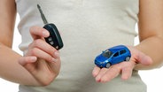 Eine Frau hält einen Autoschlüssel und ein Miniauto in den Händen. © Fotolia.com Foto: Picture-Factory