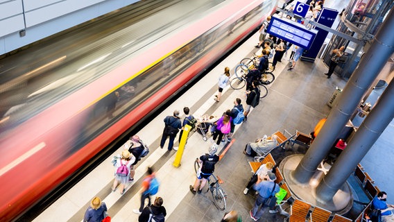 Reisende stehen an einem Bahnsteig, an dem ein Zug einfährt.  Foto: Christoph Soeder
