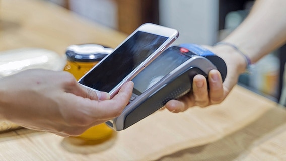 Eine Hand hält ein Smartphone an ein elektronisches Bezahlgerät. © imago images/Westend61 