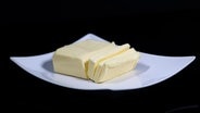 Ein Stück Butter liegt auf einem Teller vor schwarzem Hintergrund. © picture alliance/dpa/Revierfoto | Revierfoto 
