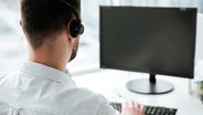 Ein Mann mit Headset sitzt vor einem Computerbildschirm und einer Tastatur © colourbox 