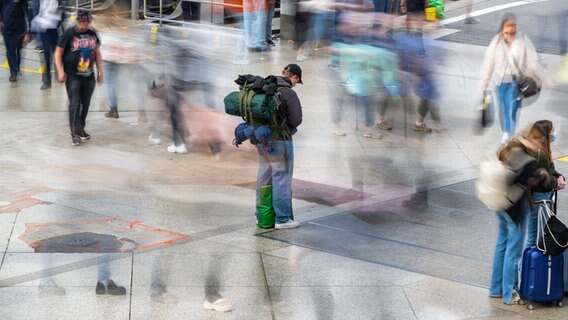 Ein Mann mit einem Rucksack steht auf einem Bahnhofsplatz, um ihn herum gehen weitere Reisende. © dpa-Bildfunk Foto: Lennart Preiss