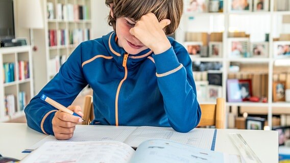 Ein Junge konzentriert sich in einem Wohnzimmer auf seine Hausaufgaben. © photocase Foto: behrchen