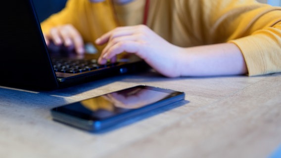 Ein Kind sitzt vor einem Laptop und einem Handy und schreibt auf der Tastatur. © photocase Foto: 2Design