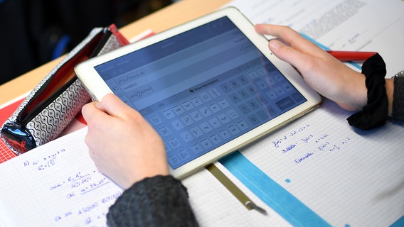 Ein Schüler hält ein Tablet in der Hand, während er Hausaufgaben macht. © picture alliance Foto: Britta Pedersen