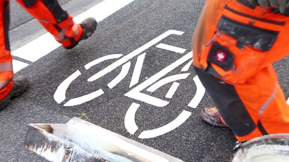Beine von Straßenarbeitern, die gerade ein Fahrradpiktogramm auf einen Radfahrstreifen aufgebracht haben. © NDR 