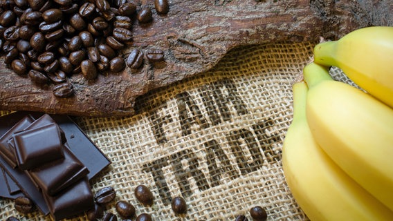 Auf einem Sack mit der Aufschrift "Fair Trade" liegen Kaffeebohnen, Bananen und Schokolade. © fotolia.com Foto: Visions-AD
