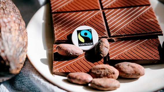 Ein Fairtrade-Siegel liegt auf Schokoladen-Stücken neben einer Kakao-Frucht. © TransFair e.V / Ilkay Karakurt 