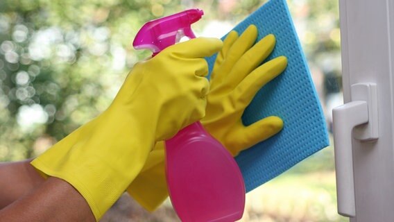 Eine Frau mit Gummihandschuhen und Sprühflasche in der Hand putzt ein Fenster mit einem Lappen. © Fotolia.com Foto: RRF
