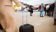 Eine Frau hat einen Handgepäcks-Koffer fest in der Hand und wartet hinter einer Schlange anderer Menschen auf dem Rollfeld darauf, in ein Flugzeug zu steigen © Colourbox Foto: Big Shot Theory