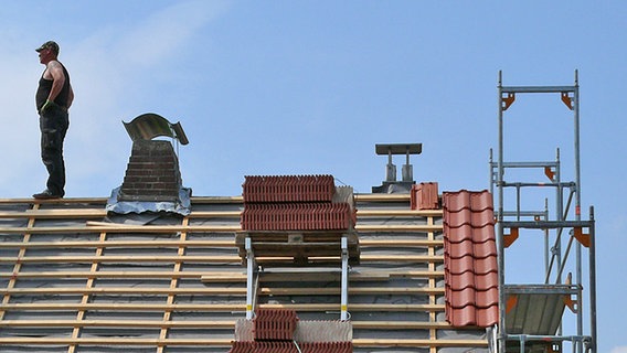 Dachdecker steht auf dem First eines ungedeckten Daches. © NDR Foto: Axel Franz