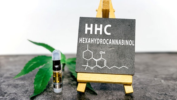 Eine Tafel mit der Aufschrift HHC Hexahydrocannabinol und einer chemischen Formel steht neben einem kleinem Fläschchen mit flüssigem HHC. © picture alliance / Zoonar | Ivan Stajkovic Foto: Ivan Stajkovic