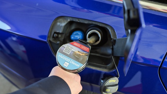 Eine Hand hält einen Stutzen mit der Aufschrift "HVO100 Diesel" in den Tank eines blauen Autos © Christian Charisius/dpa 