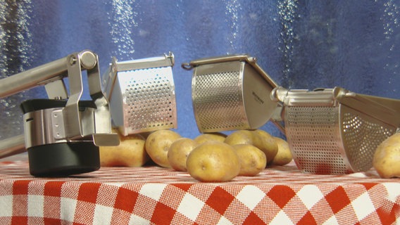 Vier verschiedene Kartoffelpressen liegen auf einem Tisch, daneben liegen einige Kartoffeln. © WDR / NDR Fernsehen 