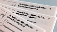 Drei Arbeitsunfähigkeitsbescheinigungen aus Papier liegen auf einem Tisch © Jens Büttner/dpa-Zentralbild/dpa Foto: Jens Büttner