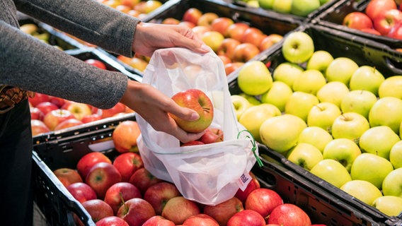 Pelanggan supermarket menempatkan apel di jaring yang dapat digunakan kembali © Picture-Alliance / Real GmbH 