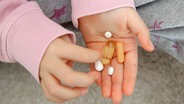 Auf der Hand eines Mädchens liegen mehrere Pillen. © picture alliance / dpa Themendienst | Mascha Brichta 