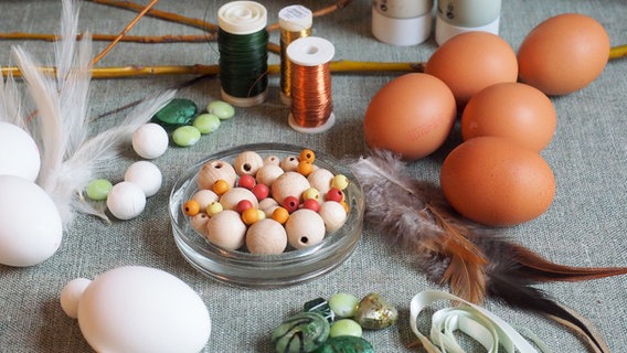 Ausgepustete Eier, Perlen aus Kunststoff und Holz, Federn, Bindedraht und Farbe liegen auf einem Tisch. © NDR Foto: Anja Deuble