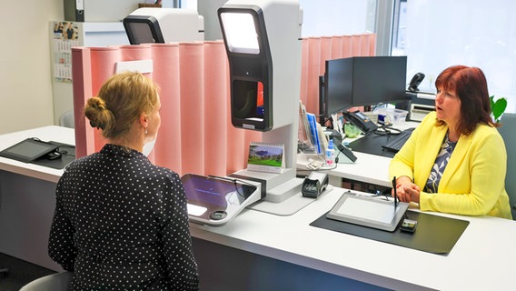 Zwei Frauen in einem Bürgeramt, das mit den technischen Geräten zur Erstellung eines digitales Passfotos ausgestattet ist. © picture alliance/dpa Foto: Jan Woitas