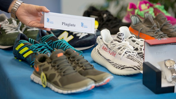 Auf einem Tisch stehen mehrere paar Schuhe, auf einem Schild steht "Plagiate". © picture alliance dpa Foto: Friso Gentsch