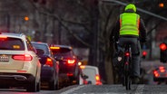 Ein Radfahrer mit reflektierender Weste im Stadtverkehr, daneben Autos. © picture alliance / dpa Themendienst Foto: Andreas Arnold