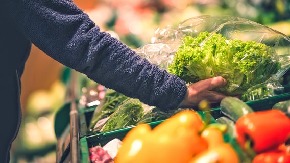 Ein Arm, der einen Salatkopf aus dem Regal in der Obst- und Gemüseabteilung eines Supermarkts nimmt. © David-W- / photocase.de Foto: David-W- / photocase.de