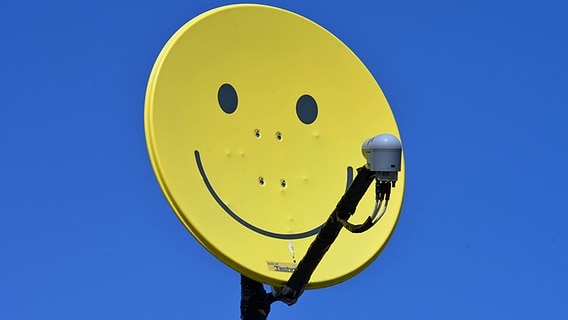 Eine Satellitenschüssel mit einem Smilie-Motiv lackiert. © imago/Schöning 