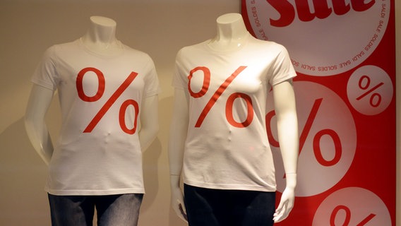 Schaufensterpuppen stehen in einem Schaufenster und tragen weiße T-Shirts mit roten Prozent-Symbolen. © picture alliance Foto: Frank May