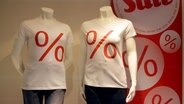 Schaufensterpuppen stehen in einem Schaufenster und tragen weiße T-Shirts mit roten Prozent-Symbolen. © picture alliance Foto: Frank May