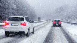 Autos fahren bei Schneetreiben auf einer verschneiten Straße.