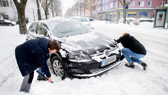 Zwei Personen entfernen Schnee vor den Rädern eines festgefahrenen Auto. © dpa Bildfunk Foto: Hauke-Christian Dittrich/dpa
