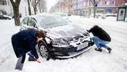 Zwei Personen entfernen Schnee vor den Rädern eines festgefahrenen Auto. © dpa Bildfunk Foto: Hauke-Christian Dittrich