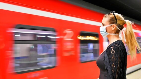 Eine Frau mit Schutzmaske steht vor einer fahrenden S-Bahn. © imago images Foto:  Michael Weber