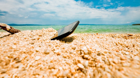 Ein Smartphone ist am Strand in den Sand gefallen. © Colourbox 
