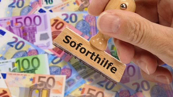 Eine Hand hält einen Stempel mit der Aufschrift "Soforthilfe" über mehrere Geldscheine. © picture alliance / Zoonar Foto: Wolfgang Filser