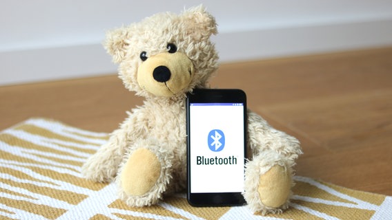 Ein Teddy mit einem Telefon, auf dem das Bluetooth-Zeichen zu sehen ist. © NDR Foto: Elke Janning