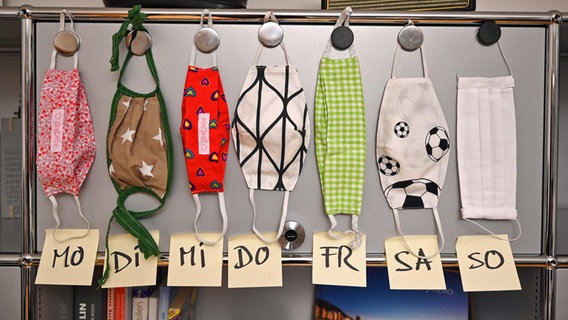 Sieben Stoffmasken hängen an einem Schrank, darunter steht jeweils ein Wochentag. © dpa Foto: Felix Kästle