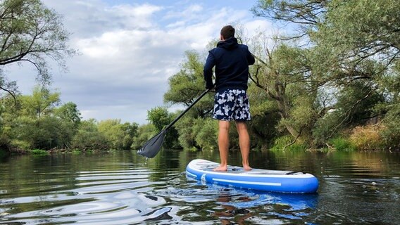 Ein Mann fährt mit einem SUP Board über einen Fluss. © dpa Foto: Julian Stratenschulte