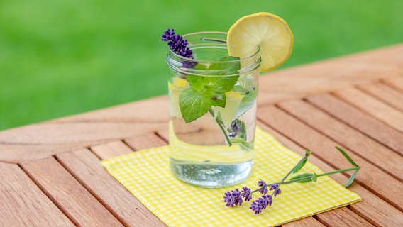 Ein Glas Wasser auf einem Holztisch mit Lavendel, Minze und Zitrone darin © NDR.de / Elke Janning Foto: Elke Janning