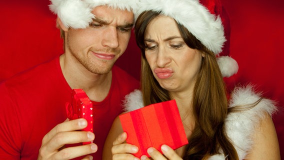 Ein Mann mit Weihnachtsmütze blickt unzufrieden auf ein Geschenk © Fotolia Foto: rubig-photo