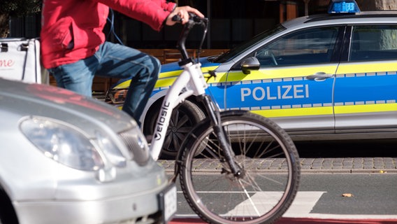 Ein Polizeiauto steht an einer Straße, davor sind ein Auto und ein Radfahrer auf einem Fahrradweg zu sehen. © dpa-Bildfunk Foto: Ole Spata