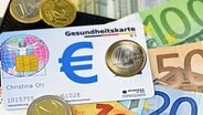 Eine Gesundheitskarte liegt auf Geldscheinen. © imago images Foto: Christian Ohde