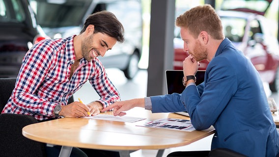 Verkäufer mit Kunden bei der Vertragsübergabe im Autohaus. © Fotolia.com Foto: luckybusiness